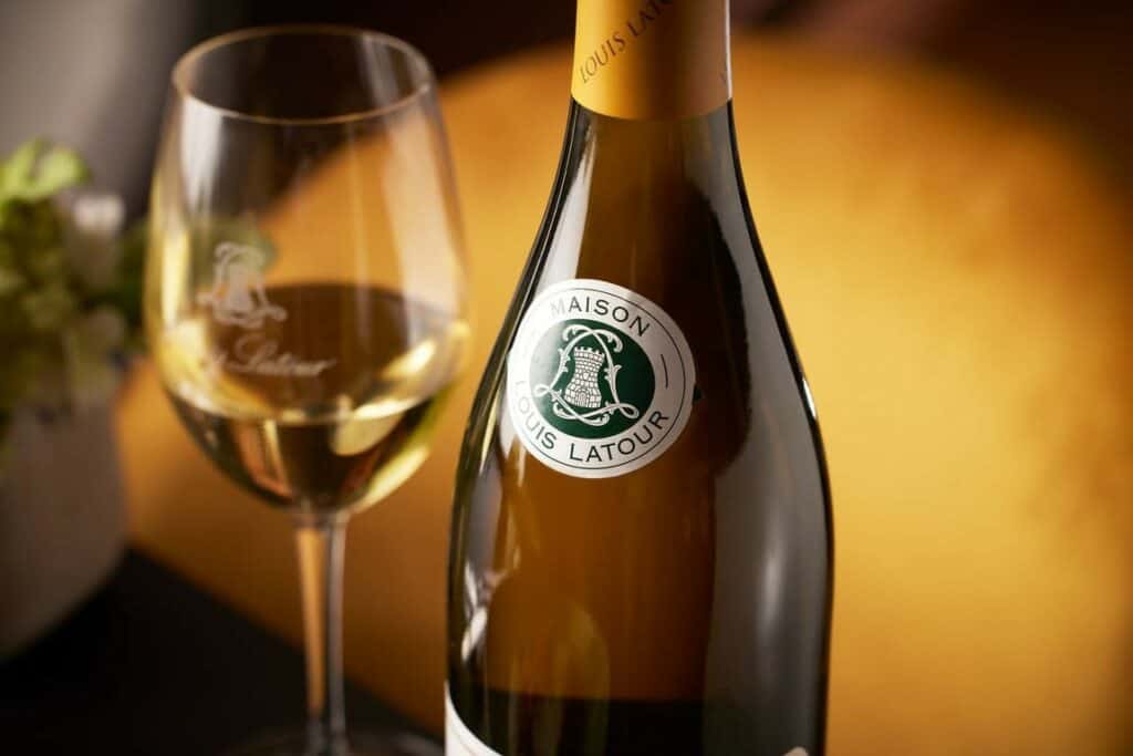 Photo of a bottle of Louis Latour white wine and a half glass of white wine. 