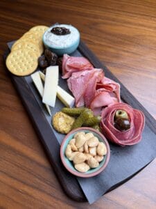 Photograph of a charcuterie plate with cured meats, cheeses, nuts, and crackers.